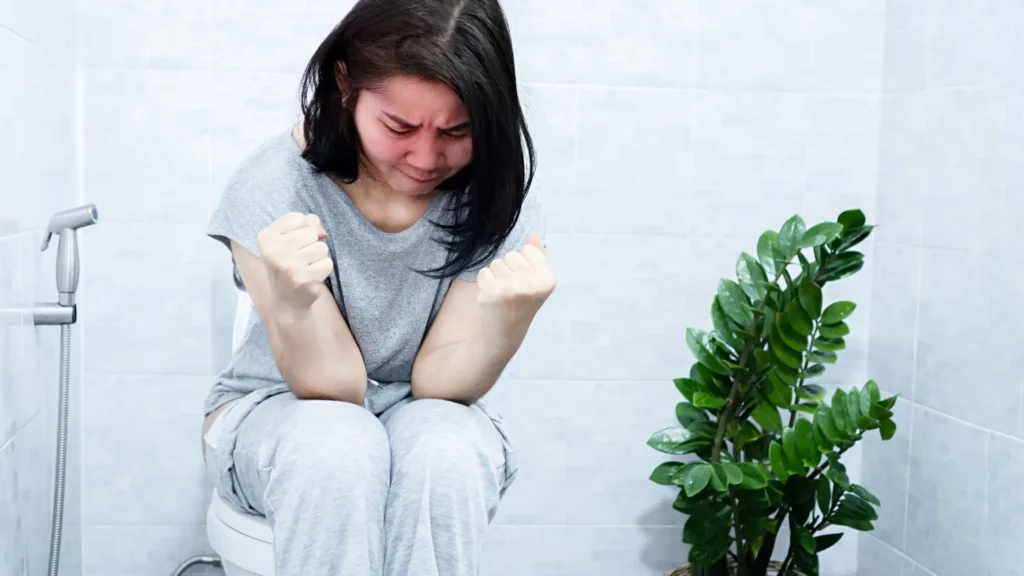 Mulher sentada no vaso sanitário com expressão de dor e com constipação