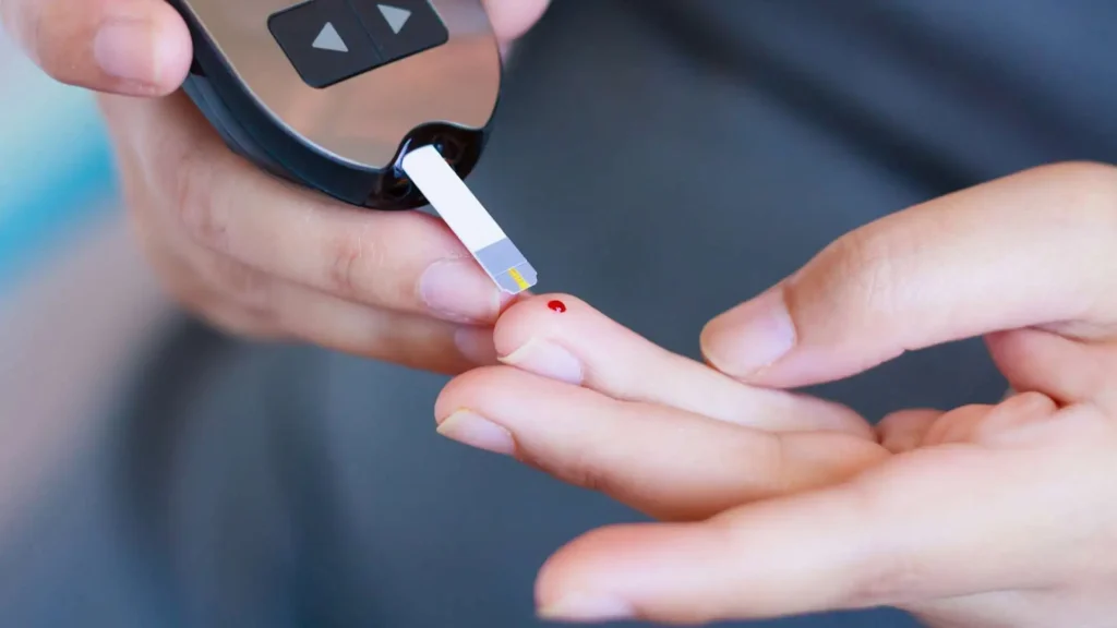 A imagem mostra uma pessoa utilizando um aparelho de controle de glicemia, faz o teste em um dos dedos para controle da diabetes