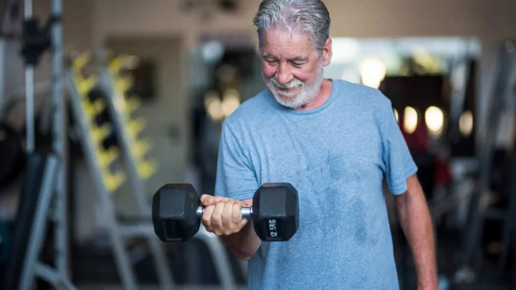 Idoso fazendo musculação treinando bíceps com peso em uma academia