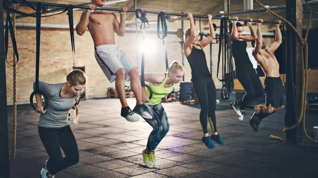 Pessoas fazendo exercícios de crossfit em uma academia, usando barra fixa e argolas.