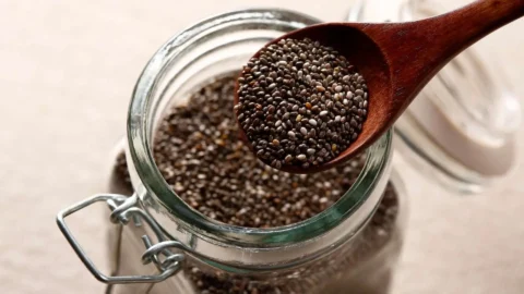 Pote de vidro transparente com sementes de chia preta e uma colher com chia em destaque