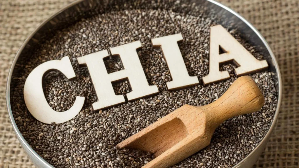 Imagem de poderosa semente de chia em tigela metálica com letras formando a palavra 'CHIA' e uma colher de pau