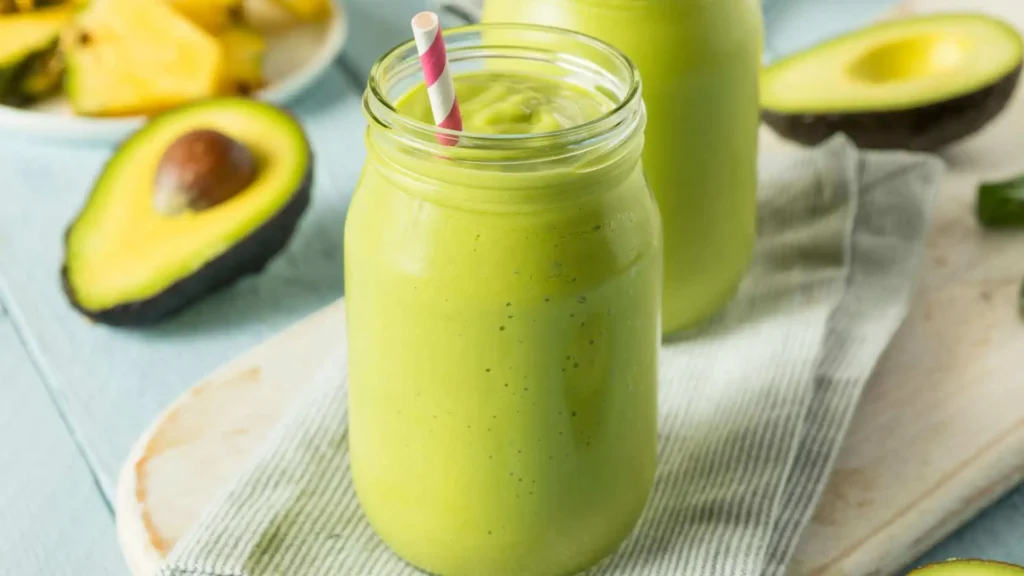 Smoothie de abacate em copo de vidro com canudo, pronto para beber, com abacate e abacaxi desfocados